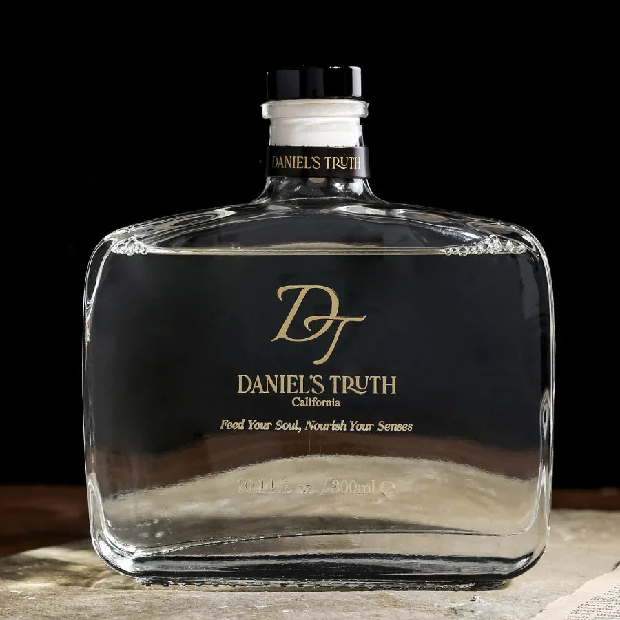 Clear glass decanter diffuser with gold Daniel's Truth logo on black background