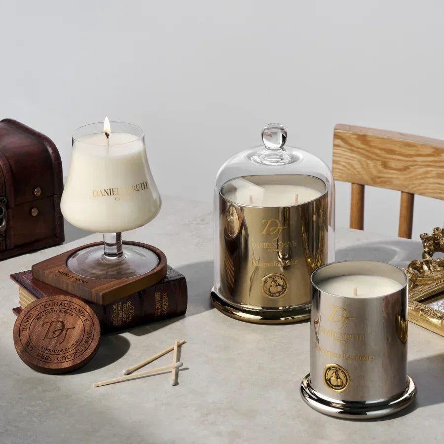 Luxury scented candles in glass holders with gold accents on a table, surrounded by books and decor.