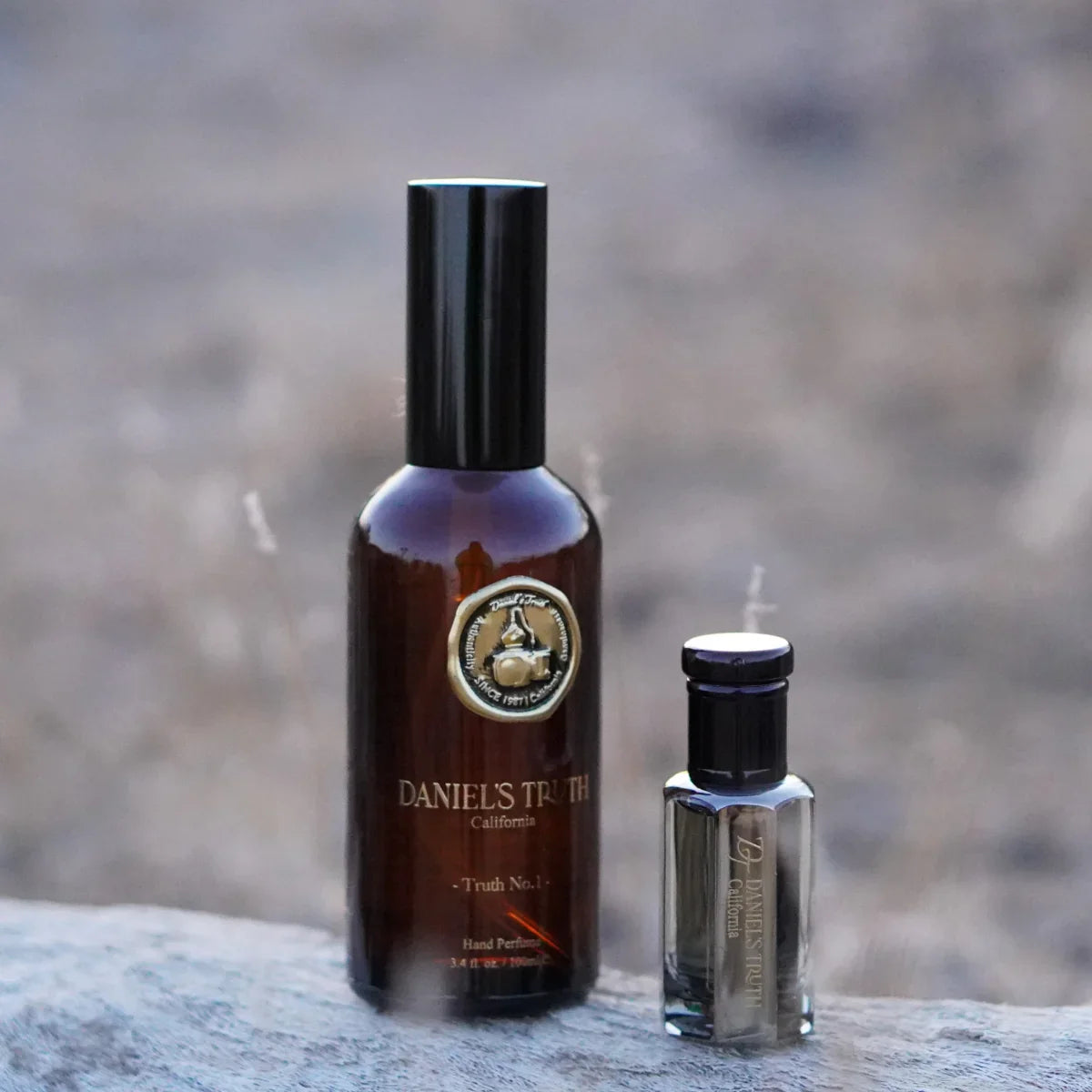 Two Daniel's Truth California perfume bottles displayed outdoors on a natural surface