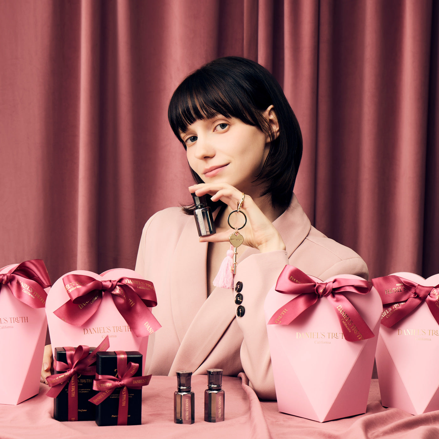 Woman in pink suit holding perfume, surrounded by pink gift boxes and perfume bottles
